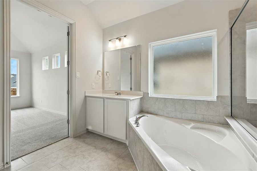 Bathroom with vanity, a bath, lofted ceiling, and light tile patterned floors Bathroom with vanity, a bath, lofted ceiling, and light tile patterned floors