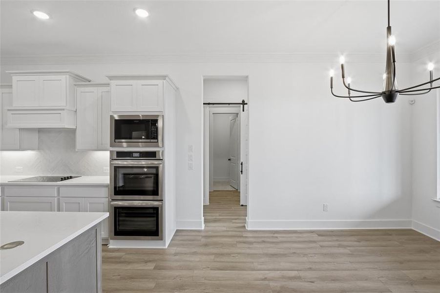 Kitchen with a barn door, white cabinets, suspended lighting, stainless steel appliances, and light wood-style floors