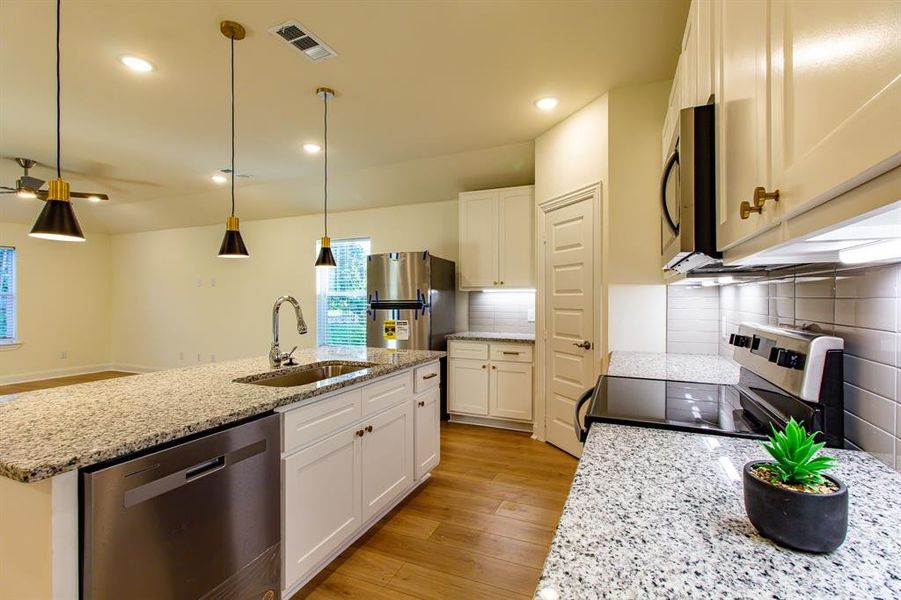 Kitchen with stainless steel appliances, light wood-style flooring, an island with sink, backsplash, and white cabinets Kitchen with stainless steel appliances, light wood-style flooring, an island with sink, backsplash, and white cabinets