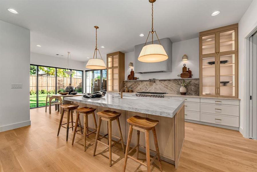 Kitchen with glass insert cabinets, a breakfast bar area, decorative backsplash, a large island, and decorative light fixtures Kitchen with glass insert cabinets, a breakfast bar area, decorative backsplash, a large island, and decorative light fixtures