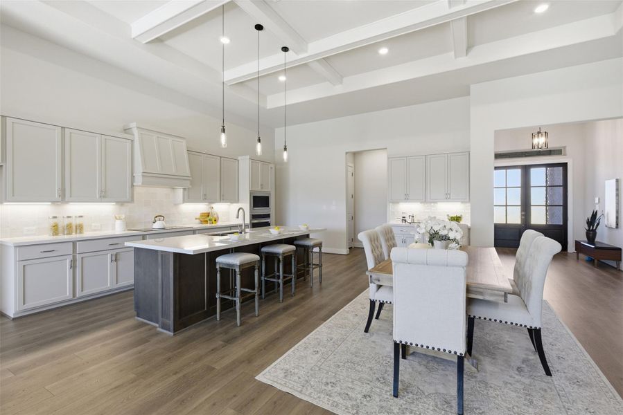 Dual tone kitchen with hanging light fixtures, backsplash, an island with sink, dark wood-style flooring, and a kitchen breakfast bar