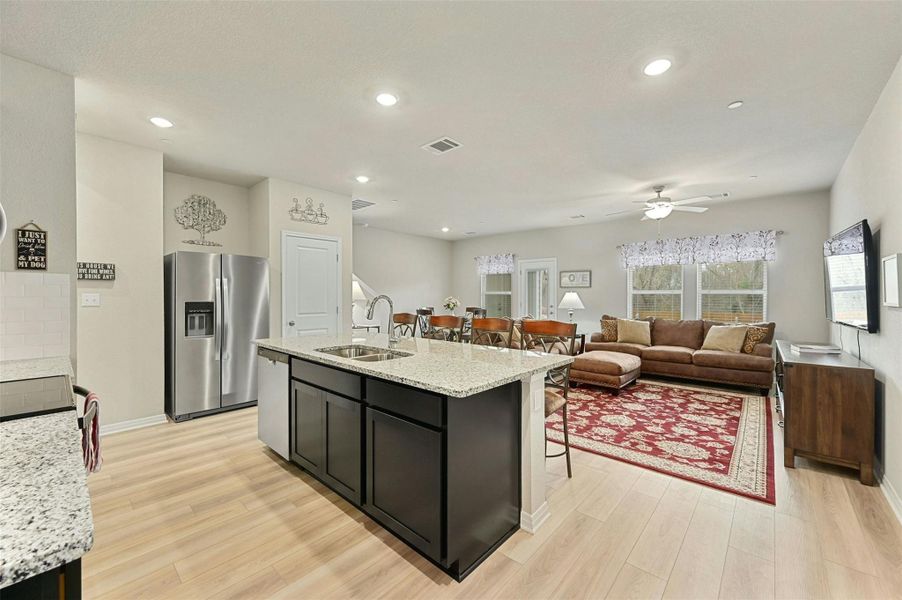 Kitchen with light stone countertops, appliances with stainless steel finishes, sink, a kitchen island with sink, and light hardwood / wood-style flooring