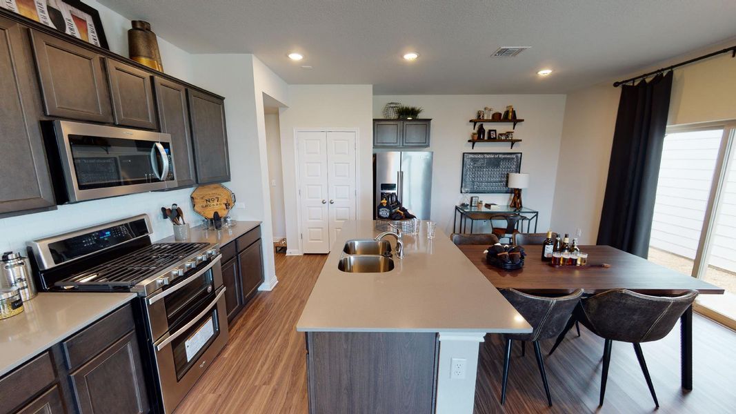 Kitchen featuring stainless steel appliances, a center island with sink, recessed lighting, light wood-type flooring, and dark wood finish cabinets