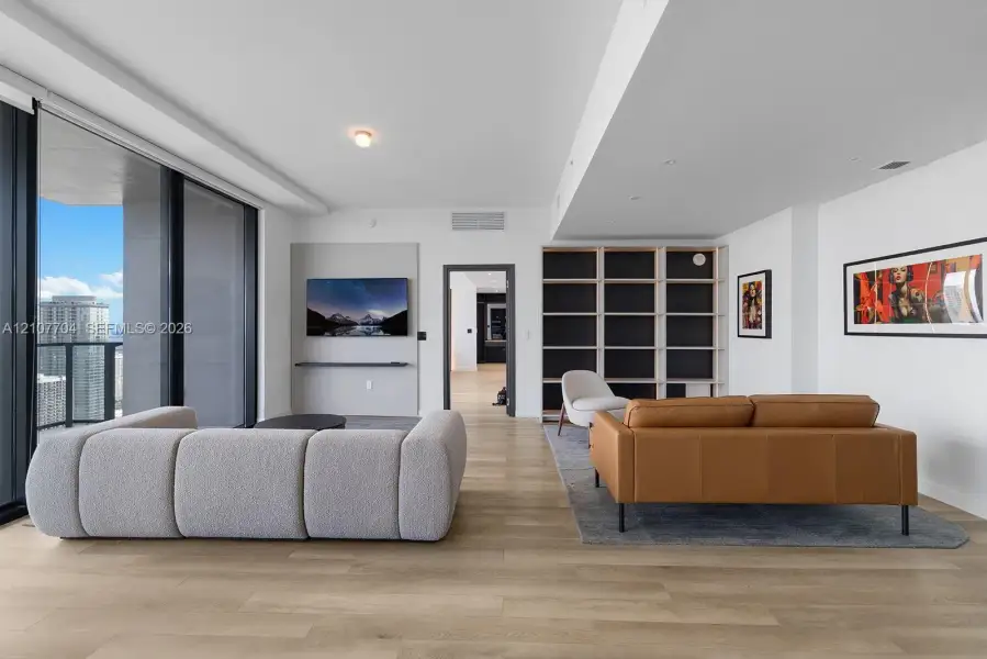 Open-concept living space featuring wood-finish flooring, floor-to-ceiling glass sliding doors, built-in floor-to-ceiling shelving, and a wall-mounted media console