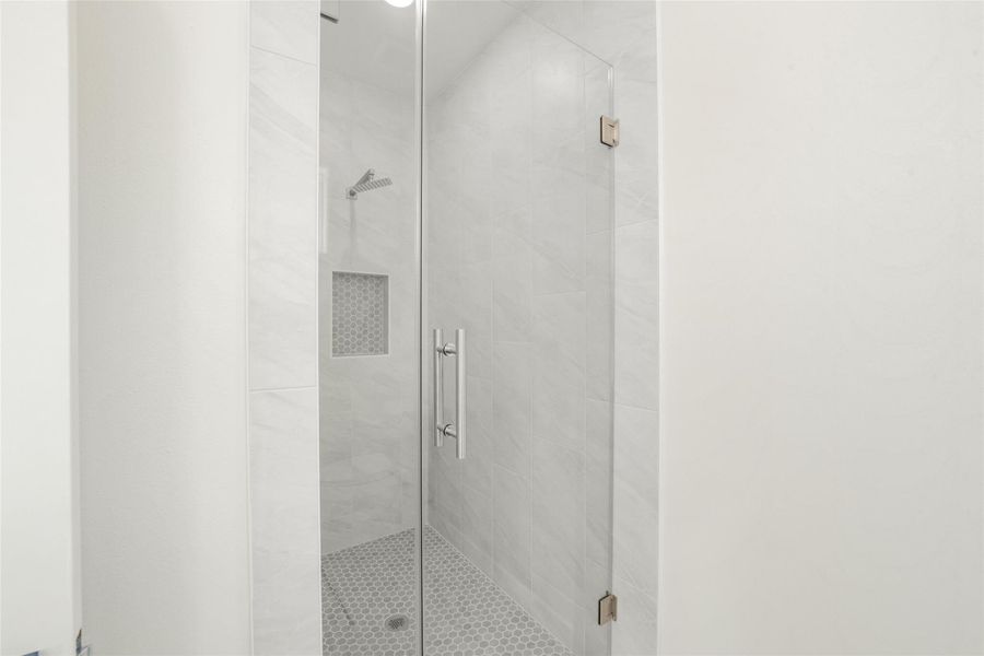 This photo shows a modern, tiled shower with a glass door, featuring a built-in niche and sleek fixtures for a clean and contemporary look.