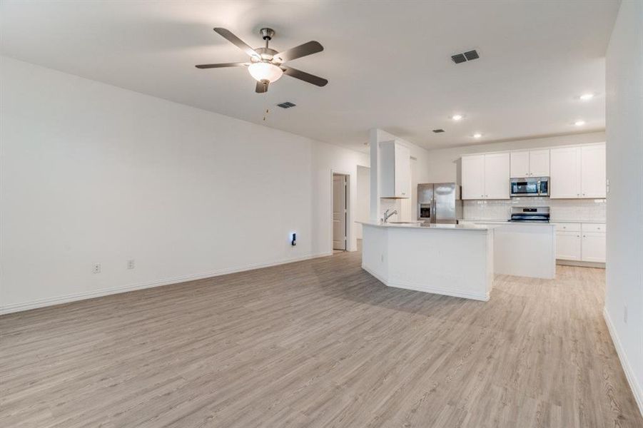 Kitchen featuring open floor plan, light countertops, white cabinets, stainless steel appliances, and a ceiling fan