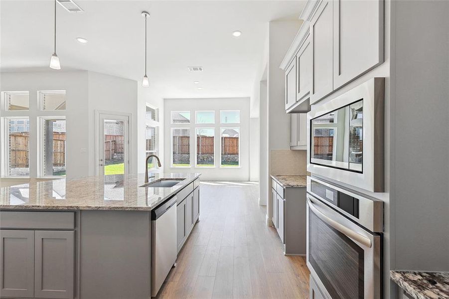 Kitchen featuring gray cabinetry, stainless steel appliances, light stone counters, and a kitchen island with sink
