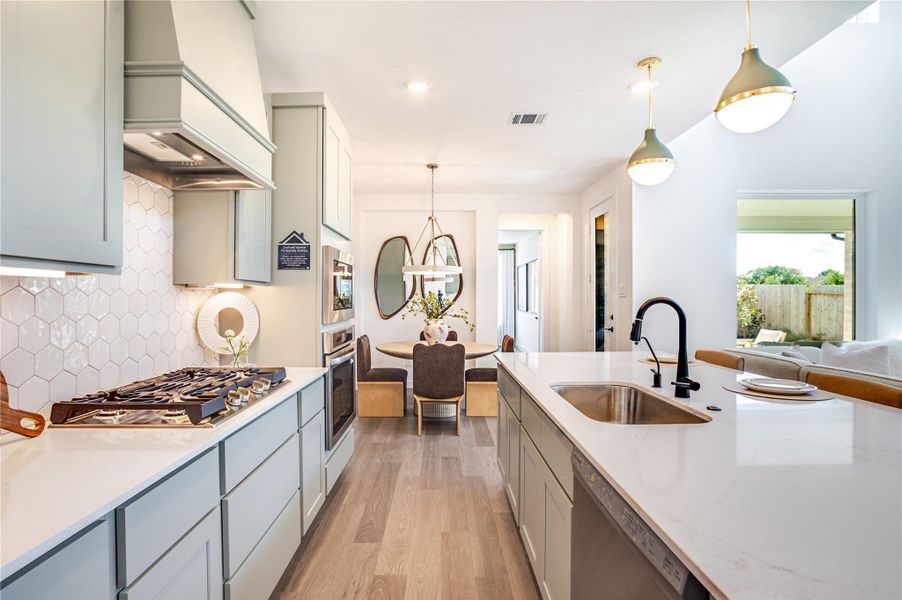 Modern kitchen with sleek cabinetry, stainless steel appliances, and a stylish hexagonal tile backsplash. An island features a sink and contemporary pendant lighting. The open layout flows into a cozy dining area with a round table, and large windows offer plenty of natural light. Modern kitchen with sleek cabinetry, stainless steel appliances, and a stylish hexagonal tile backsplash. An island features a sink and contemporary pendant lighting. The open layout flows into a cozy dining area with a round table, and large windows offer plenty of natural light.