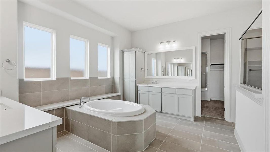 Bathroom featuring a built-in soaking tub, dual vanity with light grey cabinetry, tile flooring, and a walk-in shower with a glass enclosure