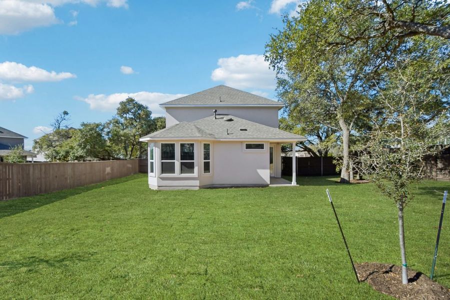 Image of the back exterior of a white two story home with a green grass back yard, a wooden fence, trees and a blue sky in the background