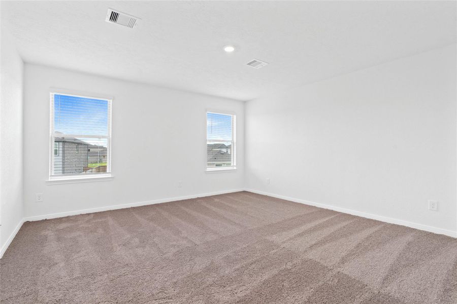 The stunning primary bedroom suite is a spacious retreat featuring plush carpeting, warm-toned walls, high ceilings, recessed lighting, and large windows with privacy blinds for comfort and tranquility.
