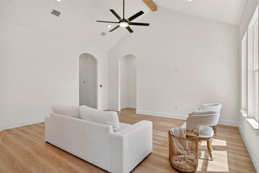 Living area featuring beamed ceiling, light wood-type flooring, high vaulted ceiling, a ceiling fan, and arched walkways