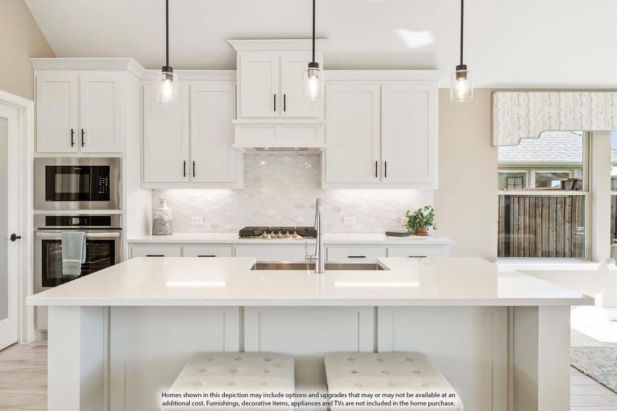 White kitchen with large island, pendant lights, tile backsplash, and stainless steel appliances White kitchen with large island, pendant lights, tile backsplash, and stainless steel appliances