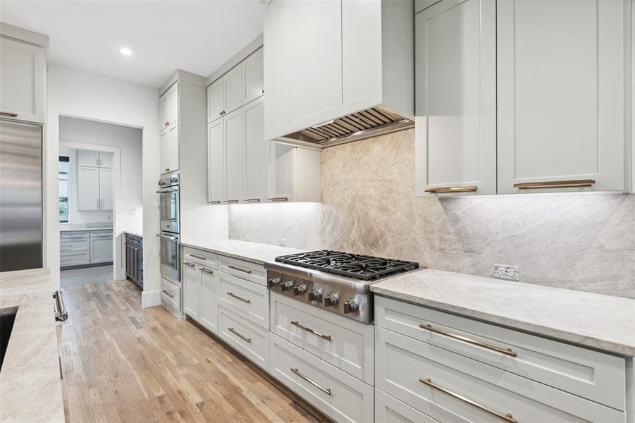 Kitchen featuring premium range hood, light stone countertops, appliances with stainless steel finishes, light hardwood / wood-style flooring, and backsplash