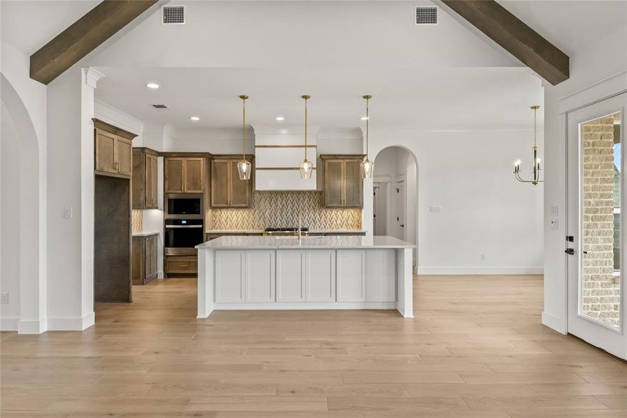 Open-concept living space featuring wood-finish flooring, exposed ceiling beams, and arched doorways