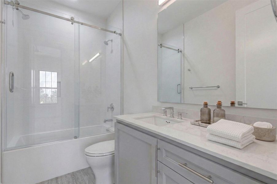 Contemporary full bath featuring a vanity, undermount sink, polished chrome fixtures, and clean tile surround. The glass-enclosed tub and shower combination includes a built-in niche for storage. Neutral finishes create a bright, spa-inspired setting consistent with the elevated design throughout the home. This photo has been virtually staged for visual reference.
