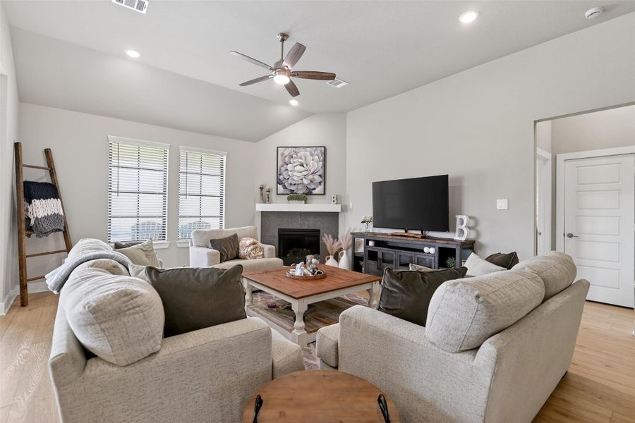 A cozy, well-lit living room with a central fireplace. The room is accented with neutral tones, and lots of natural light, enhancing the inviting atmosphere.