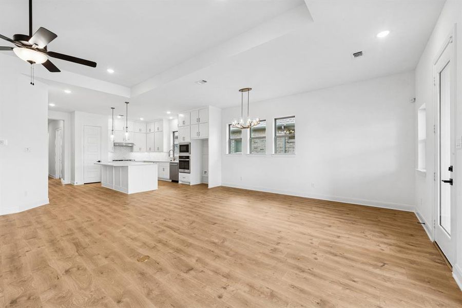 Unfurnished living room featuring ceiling fan, suspended lighting, light wood finished floors, and a tray ceiling Unfurnished living room featuring ceiling fan, suspended lighting, light wood finished floors, and a tray ceiling