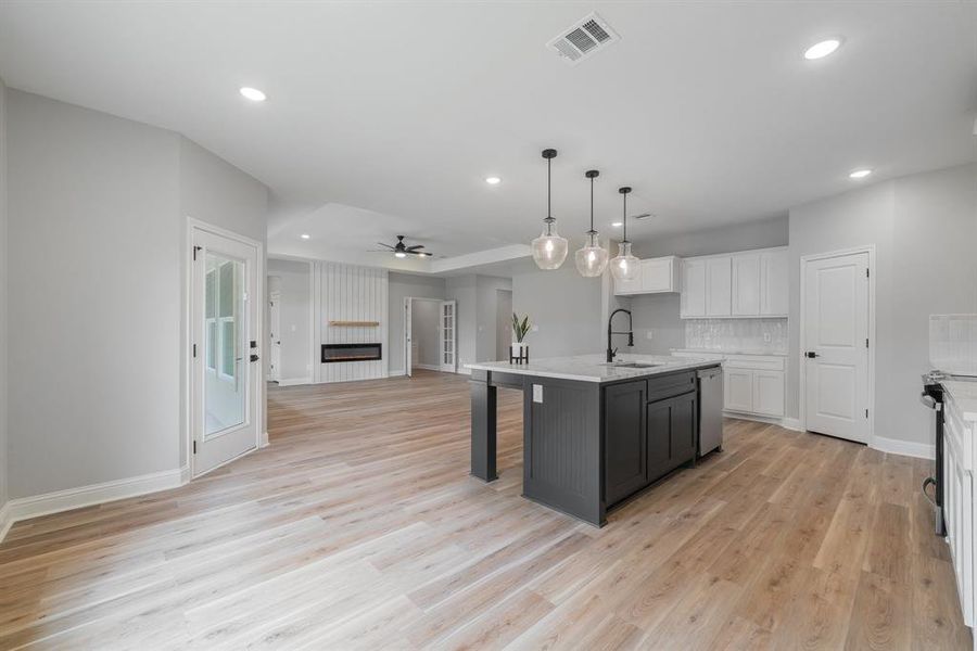 Kitchen featuring ceiling fan, light wood-type flooring, sink, white cabinets, and a kitchen island with sink