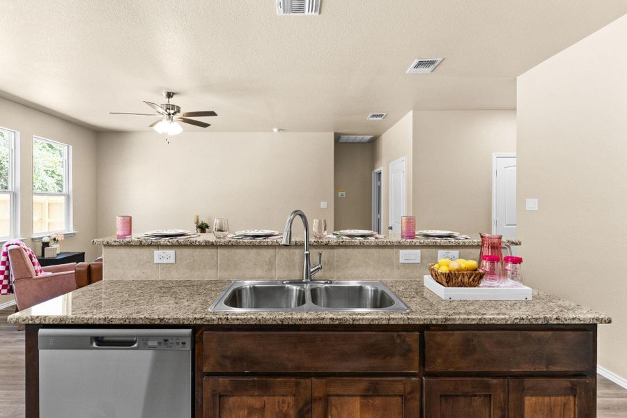 Kitchen with dark brown cabinets, light wood-type flooring, stainless steel dishwasher, open floor plan, and a ceiling fan