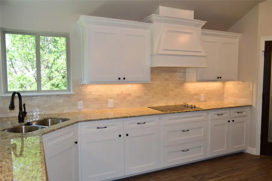 Kitchen featuring black electric stovetop, custom range hood, white cabinetry, and tasteful backsplash