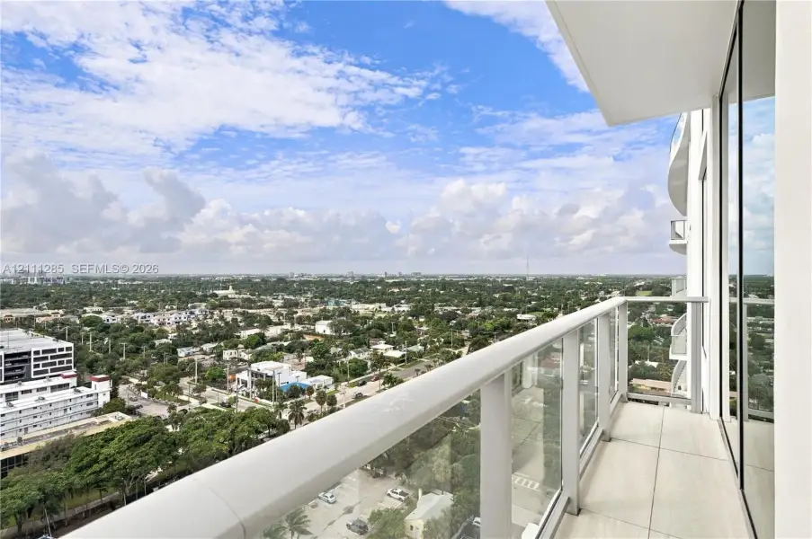 Private balcony featuring large-format tile flooring, glass panel railings, and full-height sliding glass doors Private balcony featuring large-format tile flooring, glass panel railings, and full-height sliding glass doors