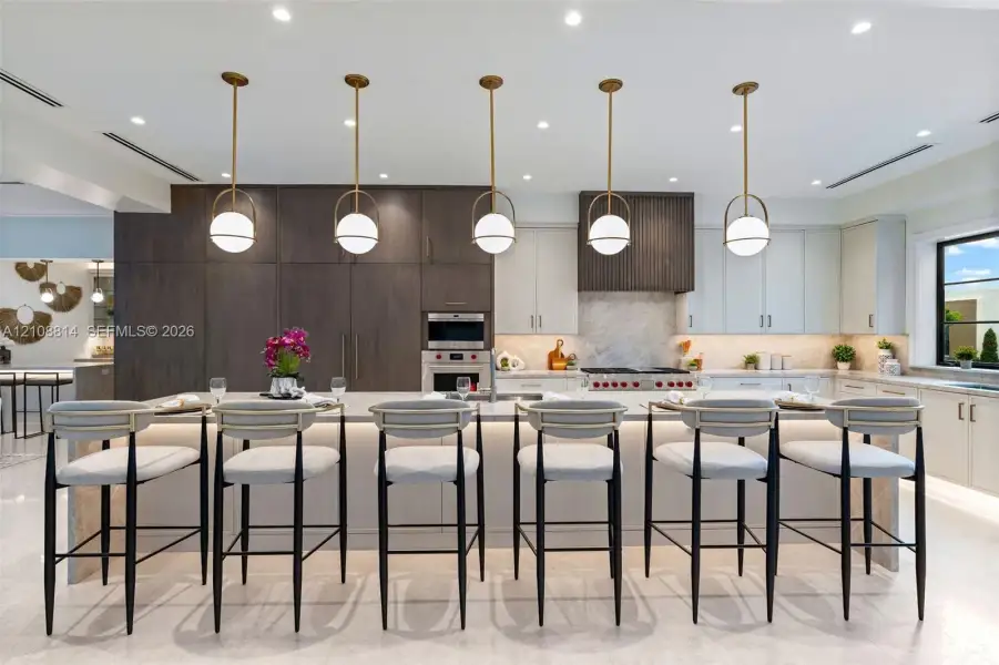 Kitchen featuring a large central island with waterfall-edge stone countertop, custom cabinetry, integrated professional-grade appliances, recessed lighting, and a series of globe-style pendant lights Kitchen featuring a large central island with waterfall-edge stone countertop, custom cabinetry, integrated professional-grade appliances, recessed lighting, and a series of globe-style pendant lights