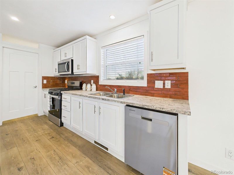 This spacious kitchen highlights the functionality of extended countertop space, paired with bar seating, sleek white cabinetry, and stainless steel appliances for a clean, modern finish.