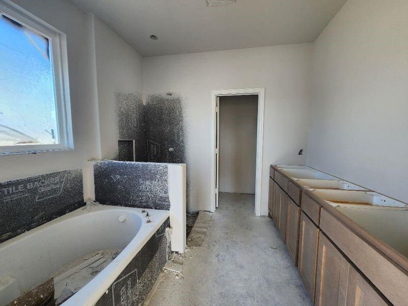 Bathroom featuring double vanity, a garden tub, walk in shower, and unfinished concrete flooring
