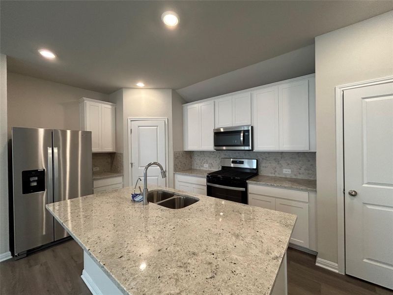 Kitchen with stainless steel appliances, dark wood-type flooring, white cabinets, tasteful backsplash, and a kitchen island with sink Kitchen with stainless steel appliances, dark wood-type flooring, white cabinets, tasteful backsplash, and a kitchen island with sink