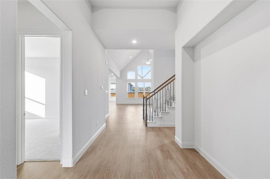 Corridor with lofted ceiling, light wood-style flooring, stairs, and recessed lighting Corridor with lofted ceiling, light wood-style flooring, stairs, and recessed lighting
