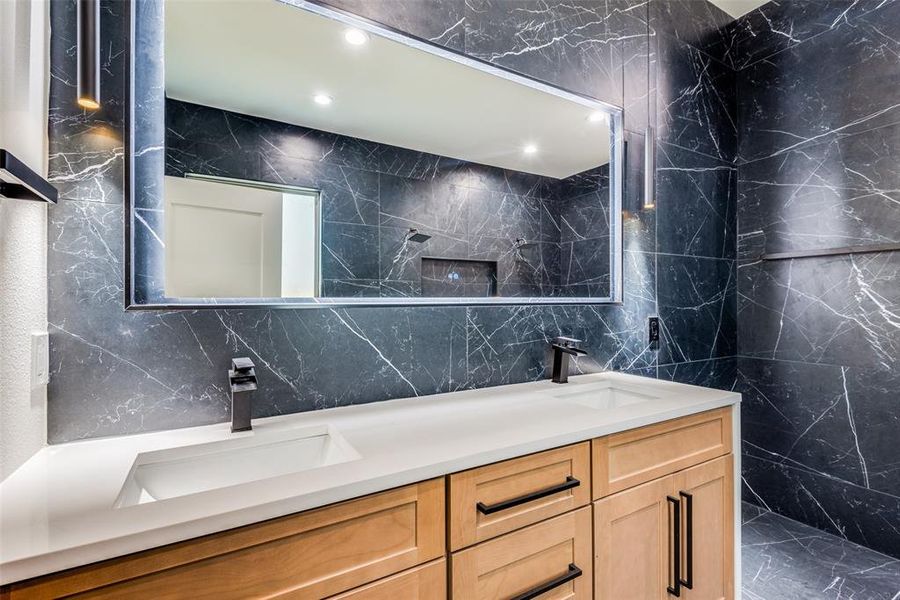 Bathroom with vanity, a tile shower, and tile walls