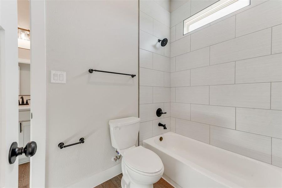 Bathroom with hardwood / wood-style floors, tiled shower / bath combo, and toilet