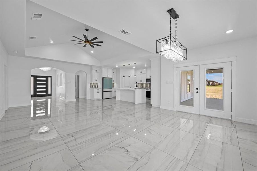 Unfurnished living room with ceiling fan with notable chandelier, french doors, high vaulted ceiling, and light tile patterned floors