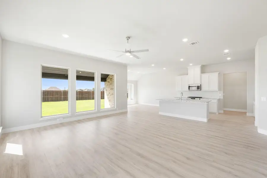 Open-concept living area with light wood floors, ceiling fan, and kitchen island with white cabinets in background.