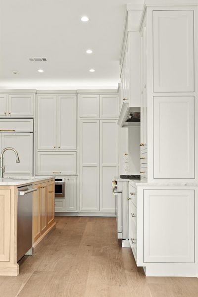 Kitchen featuring premium appliances, light countertops, a sink, light wood-type flooring, and recessed lighting