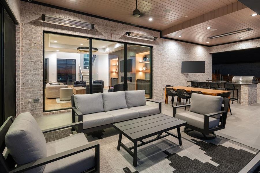 Exceptional covered outdoor living space designed for luxury entertaining, featuring a stunning wood-paneled ceiling with recessed lighting, built-in speakers, and patio heaters. The fully equipped outdoor kitchen includes a premium grill, sink, refrigerator, and expansive prep space, all complemented by a mounted TV for the ultimate indoor-outdoor living experience.