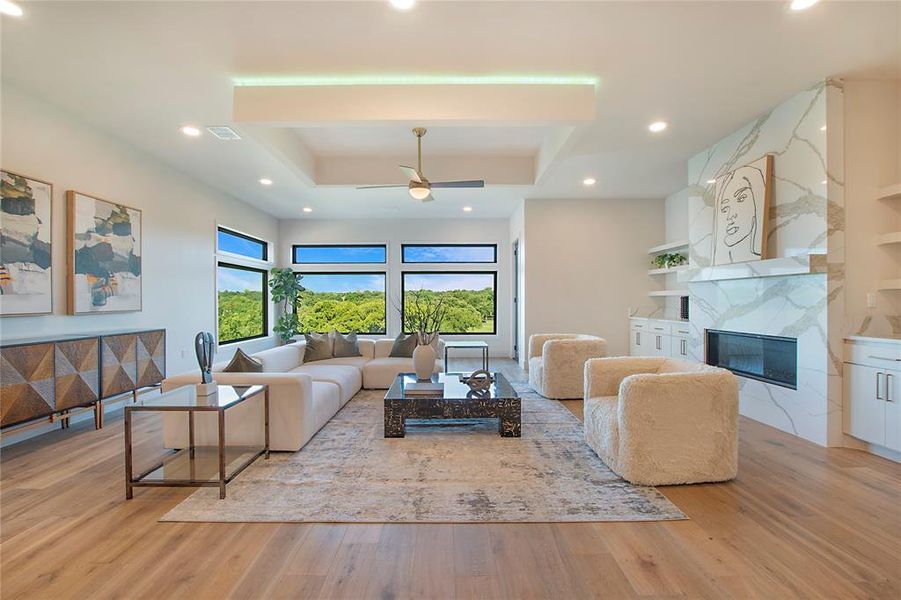 Living room with a fireplace, ceiling fan, a tray ceiling, built in shelves, and light wood-type flooring