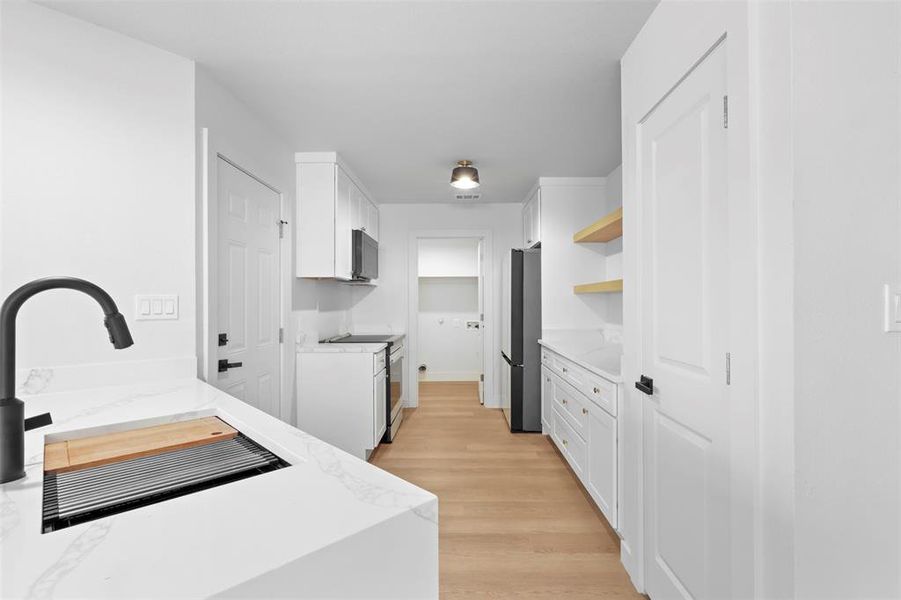 Kitchen with appliances with stainless steel finishes, white cabinets, and light stone counters