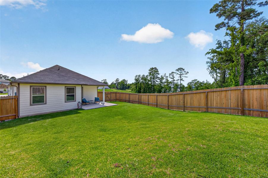 This photo showcases a spacious backyard with a well-maintained lawn, a wooden fence for privacy, and a small covered patio area attached to a single-story house. Ideal for outdoor activities and relaxation. This photo showcases a spacious backyard with a well-maintained lawn, a wooden fence for privacy, and a small covered patio area attached to a single-story house. Ideal for outdoor activities and relaxation.