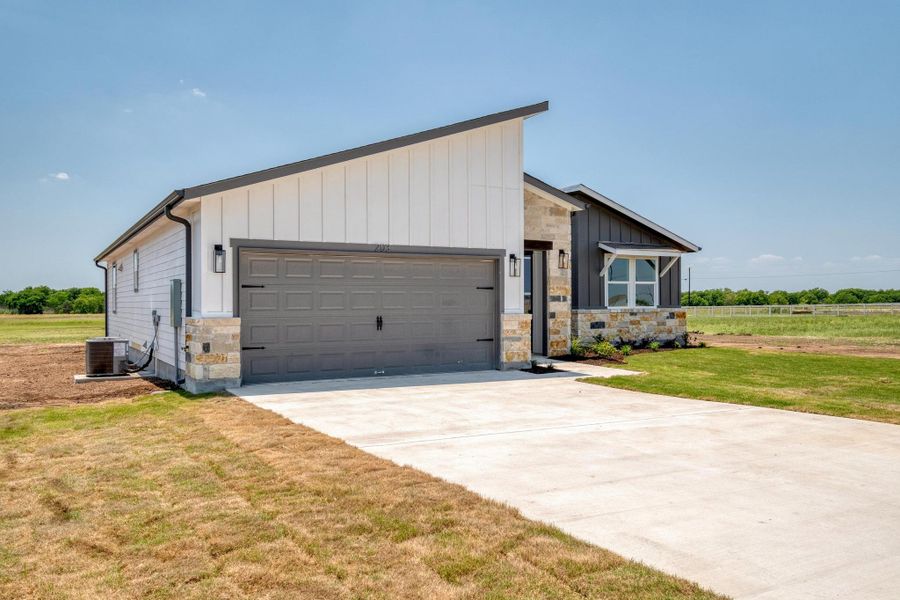 View of front of house with stone siding, an attached garage, concrete driveway, central air condition unit, and a front lawn