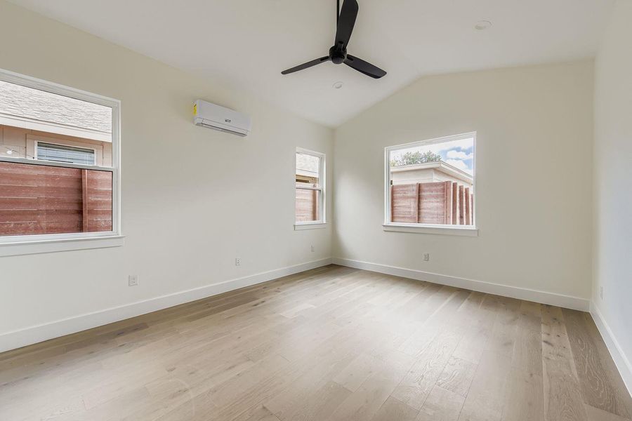 Unfurnished room featuring lofted ceiling, light wood finished floors, a wall mounted air conditioner, and ceiling fan Unfurnished room featuring lofted ceiling, light wood finished floors, a wall mounted air conditioner, and ceiling fan