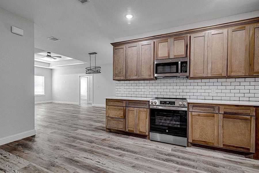 Kitchen featuring stainless steel appliances, pendant lighting, light hardwood / wood-style floors, decorative backsplash, and ceiling fan