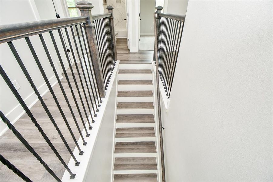 This is a modern staircase with white risers, stylish wood-look treads, and an elegant dark metal baluster railing system, providing a sleek, contemporary transition between floors.