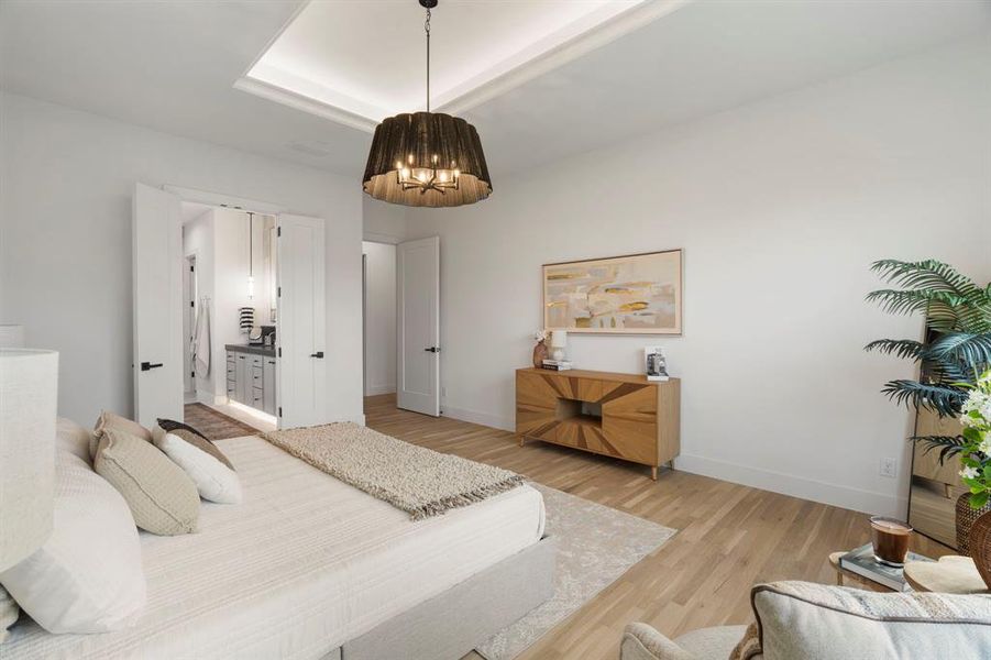 Bedroom with ensuite bathroom, a raised ceiling, and light wood-type flooring Bedroom with ensuite bathroom, a raised ceiling, and light wood-type flooring