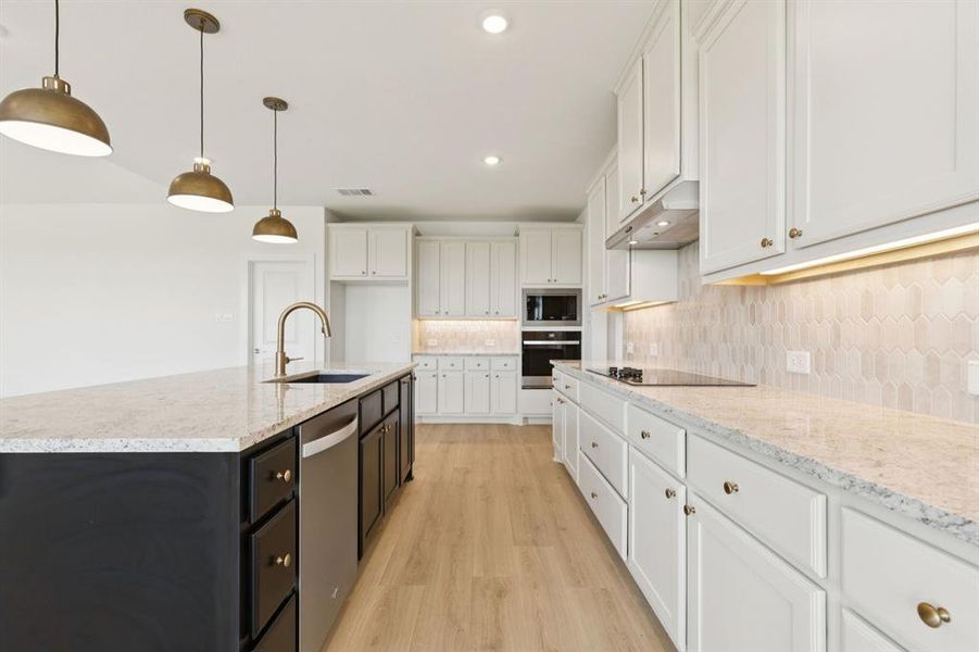 Kitchen featuring white cabinets, backsplash, decorative light fixtures, light wood-style floors, and light stone countertops