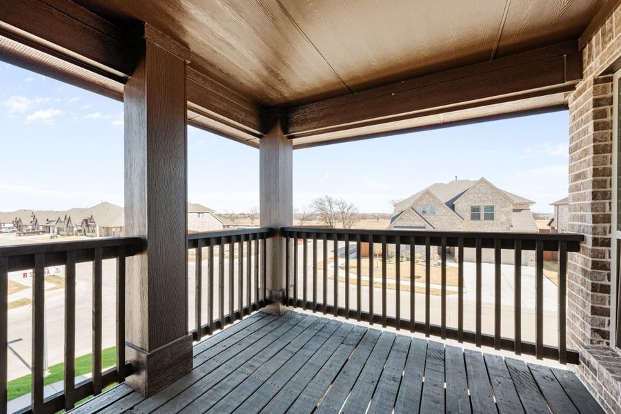 Covered second-floor balcony with dark wood railings and deck overlooking a residential neighborhood street