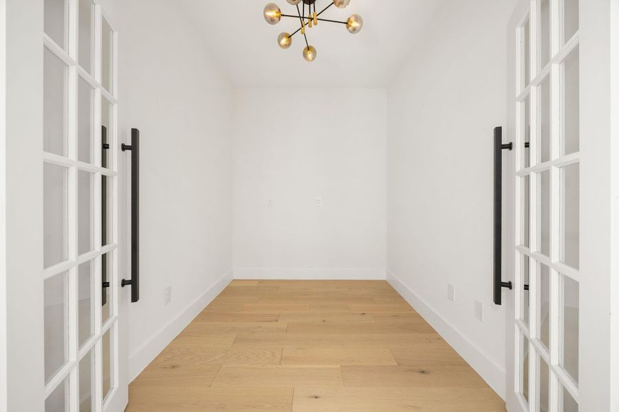 Elegant double doors open to a versatile home office or flex space, featuring a stylish light fixture and a bright, inviting atmosphere.