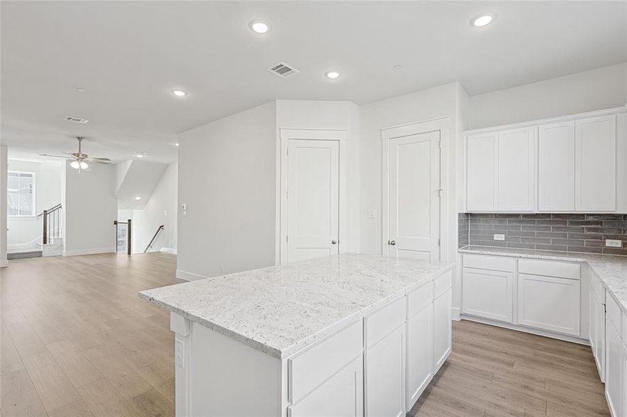 Kitchen featuring an island with a light-colored countertop, white cabinetry, and a gray subway tile backsplash