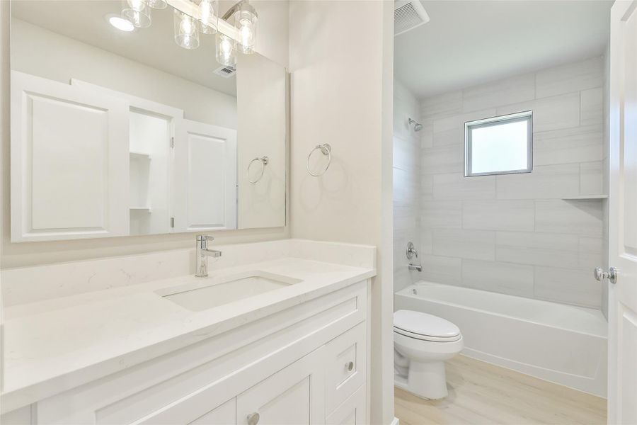 The full guest bath features a sleek vanity with quartz counters, built-in storage, and a soaking tub with modern tile surround and an accent window.